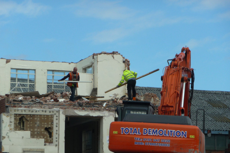 Workers clamber over rubble on the partially demolished building