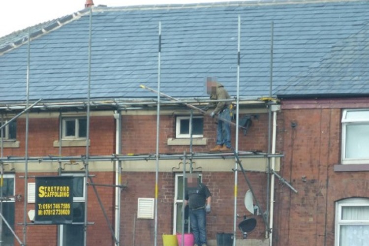 Workers on unsafe scaffolding outside a row of terraced shops in Oldham